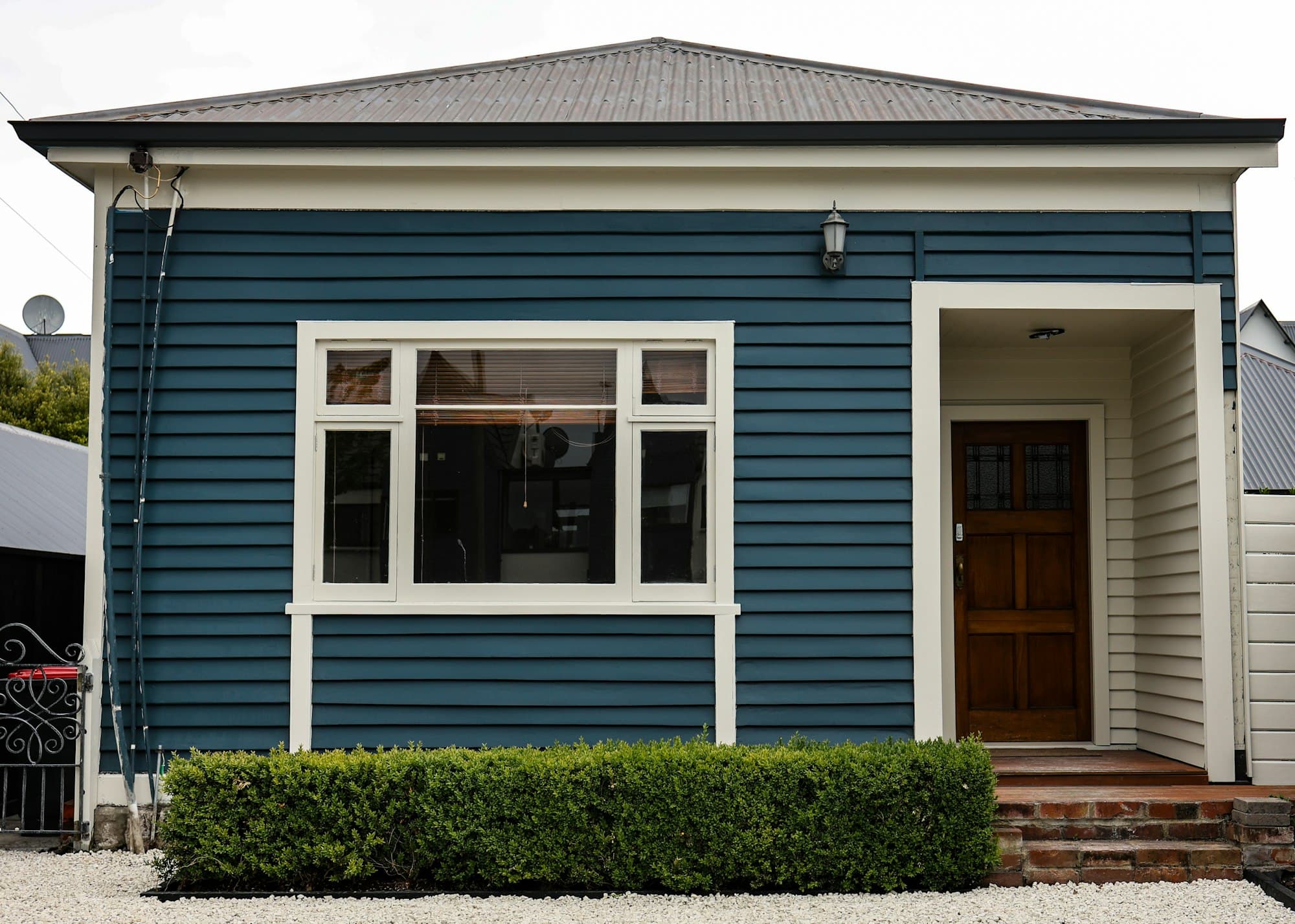 Tidy blue weatherboard New Zealand home with a clipped hedge and a freshly painted exterior